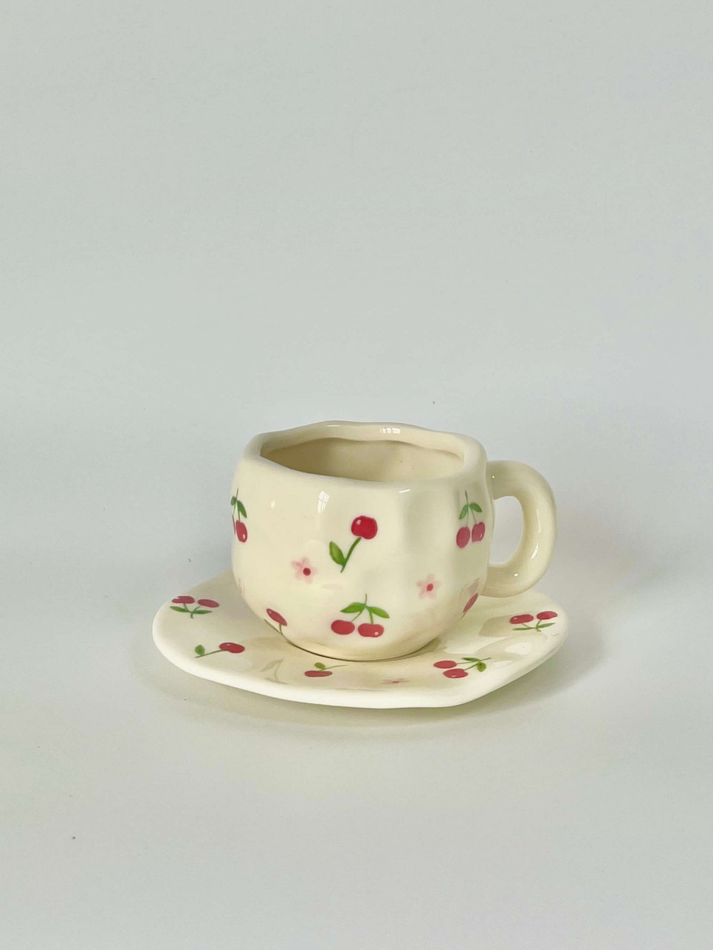 Cute blue cherry tea set with mug and saucer together. Adorable beige background with hand painted red cherry accents drawing on. Coquette girl aesthetic. Perfect gift for mums, daughters and girlfriends. Cafe vibes at home.