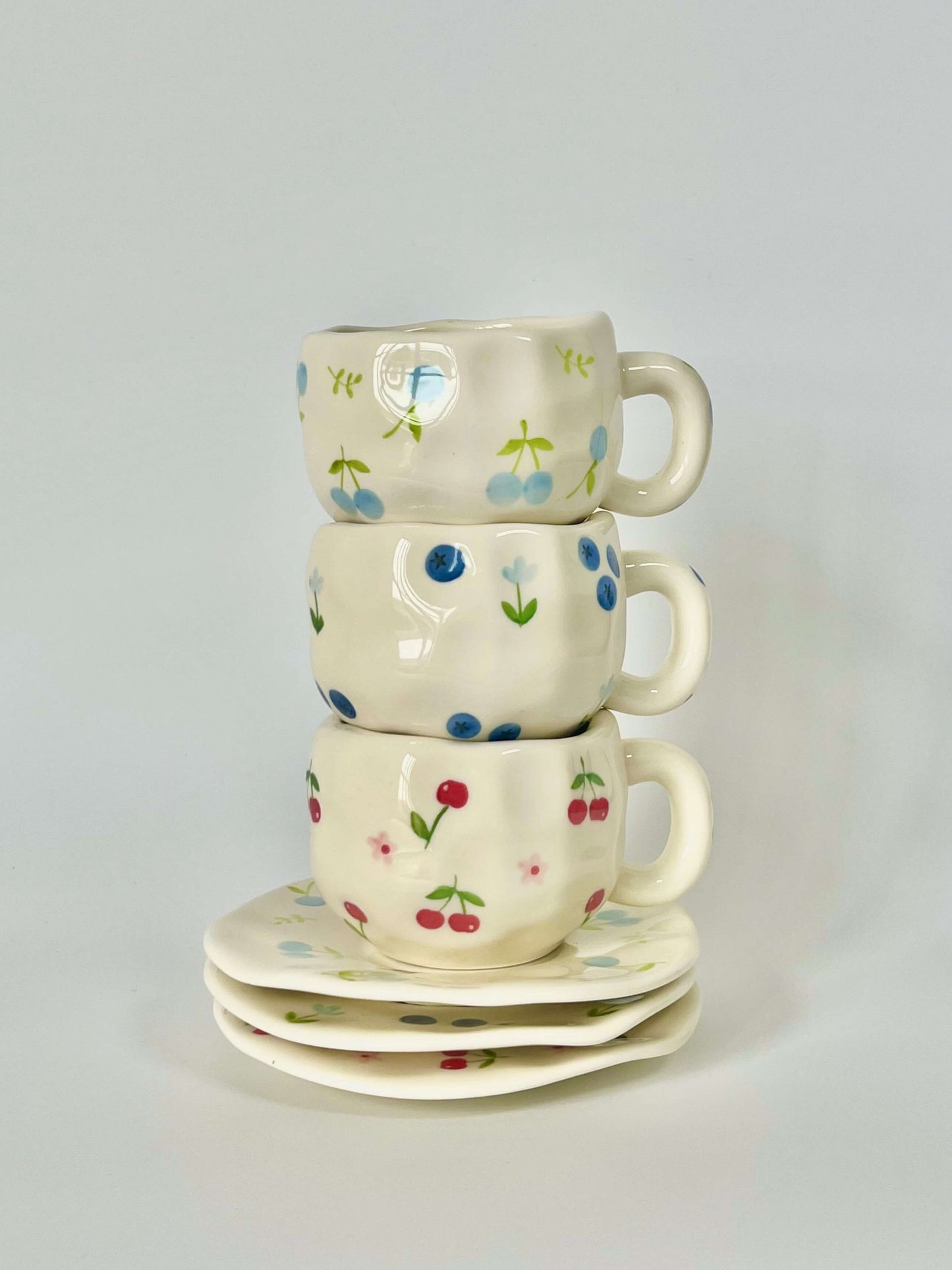 Cute blue cherry tea set with mug and saucer together. Adorable beige background with hand painted blue cherry accents drawing on. Coquette girl aesthetic. Perfect gift for mums, daughters and girlfriends. Cafe vibes at home.