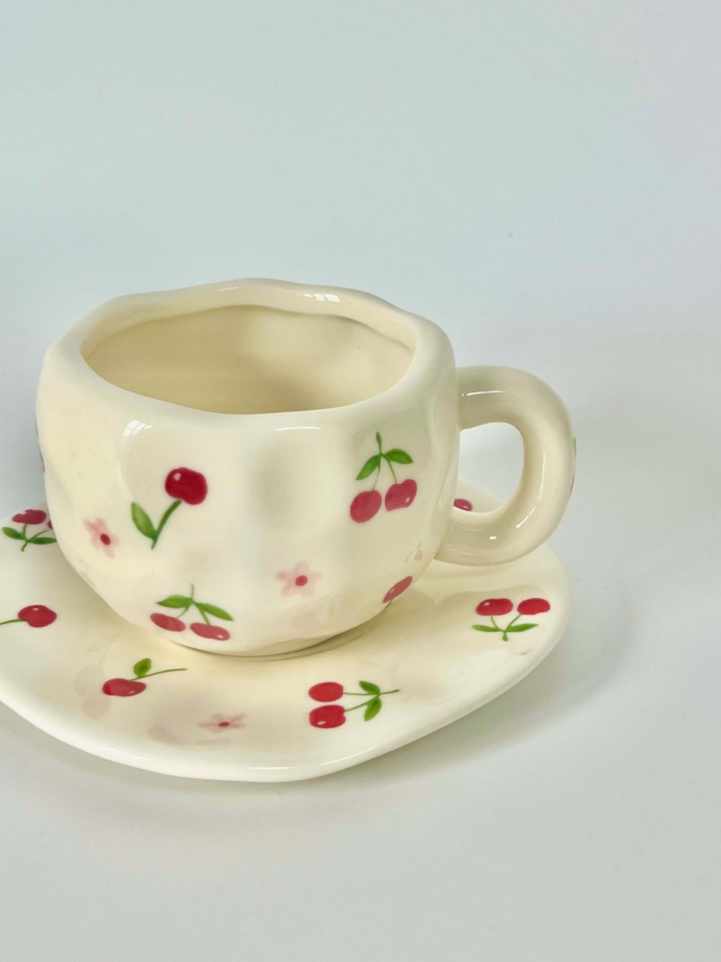 Cute blue cherry tea set with mug and saucer together. Adorable beige background with hand painted red cherry accents drawing on. Coquette girl aesthetic. Perfect gift for mums, daughters and girlfriends. Cafe vibes at home.