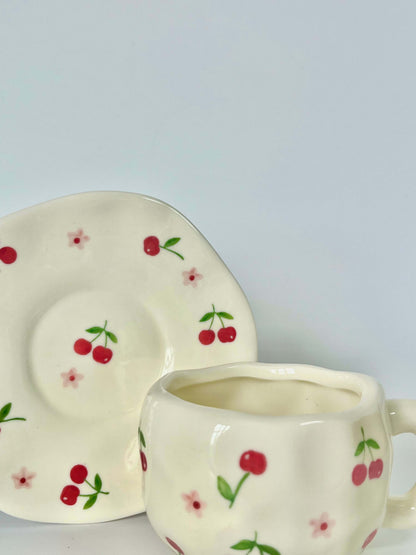 Cute blue cherry tea set with mug and saucer together. Adorable beige background with hand painted red cherry accents drawing on. Coquette girl aesthetic. Perfect gift for mums, daughters and girlfriends. Cafe vibes at home.